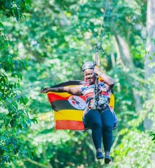 A lady on a Ziplining adventure through the Mabira Forest Canopy waving a Ugandan Flag